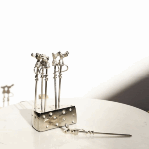 A close-up of metal skewers standing in a shiny holder with a white background.